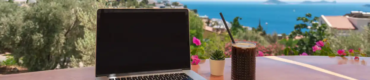 A view of a laptop and an ice drink with a beach in the background