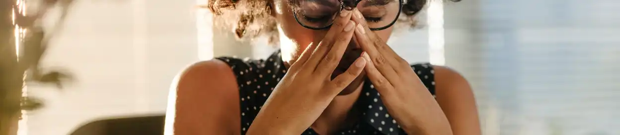 A woman with glasses puts her hands to her face in a manner depicting stress