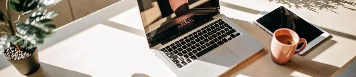 a desk with a plant, a laptop computer, a coffee mug and a tablet computer