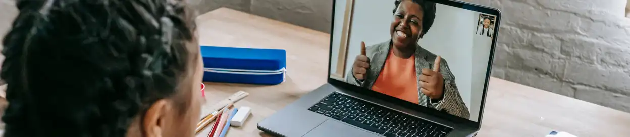 An online English lesson - the teacher is on a laptop screen giving a double thumbs-up